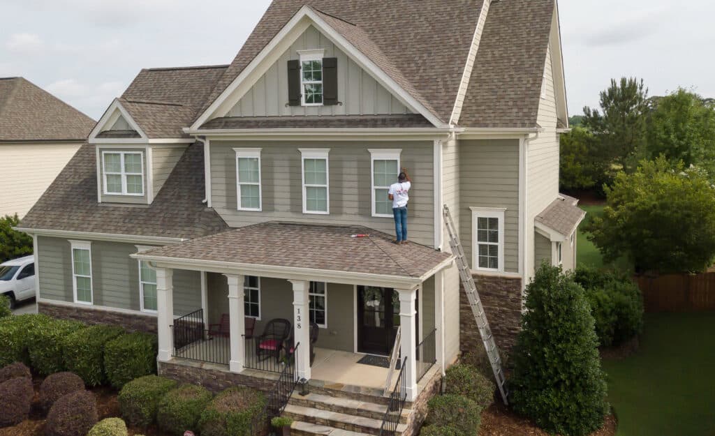 Oak City Coatings painter on a ladder during an exterior repaint of a two-story Raleigh-area home