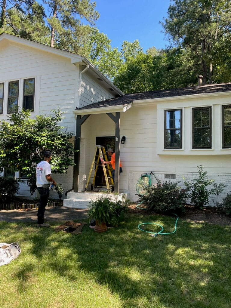 Oak city coatings team members standing on a ladder in front of a house while working on exterior painting