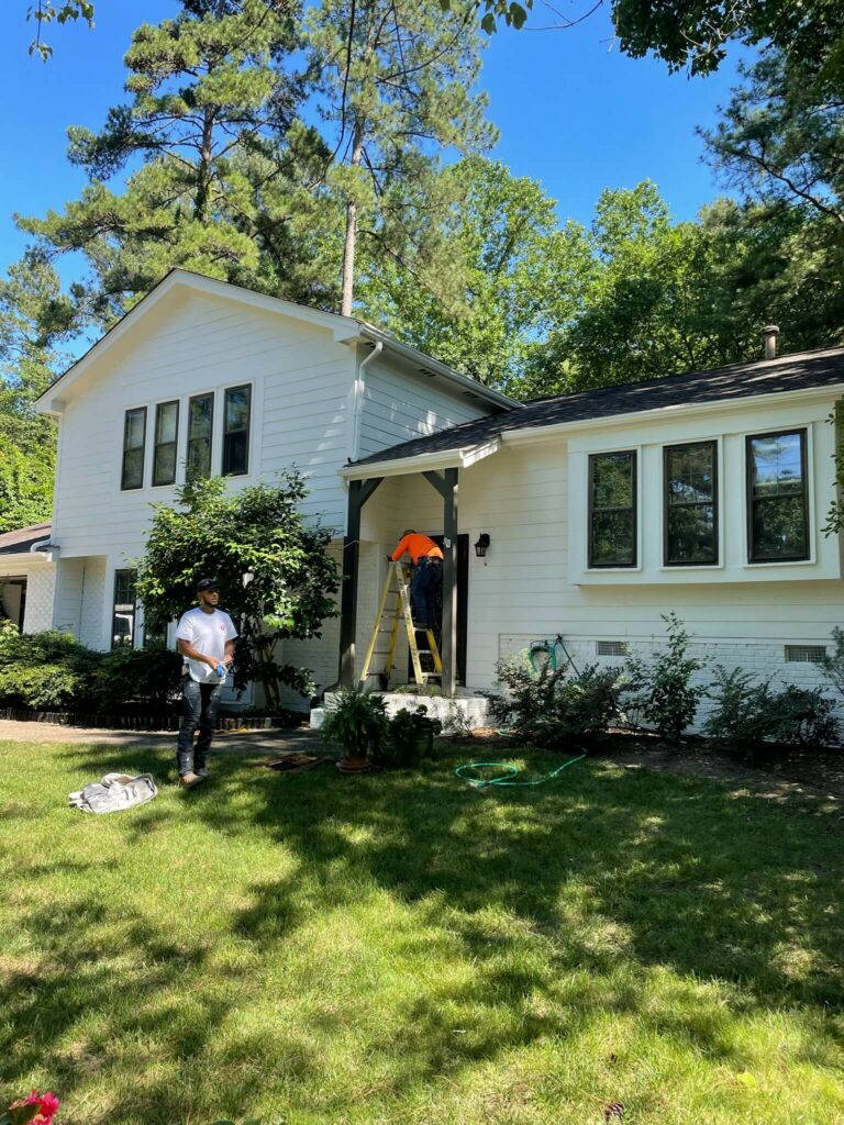 Oak city coatings team member standing on a ladder in front of a house while team is repainting exterior