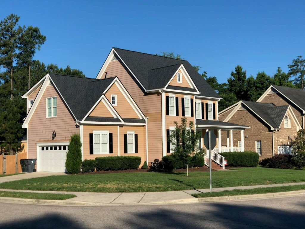 Two-story home with tan siding before an Oak City Coatings exterior repaint