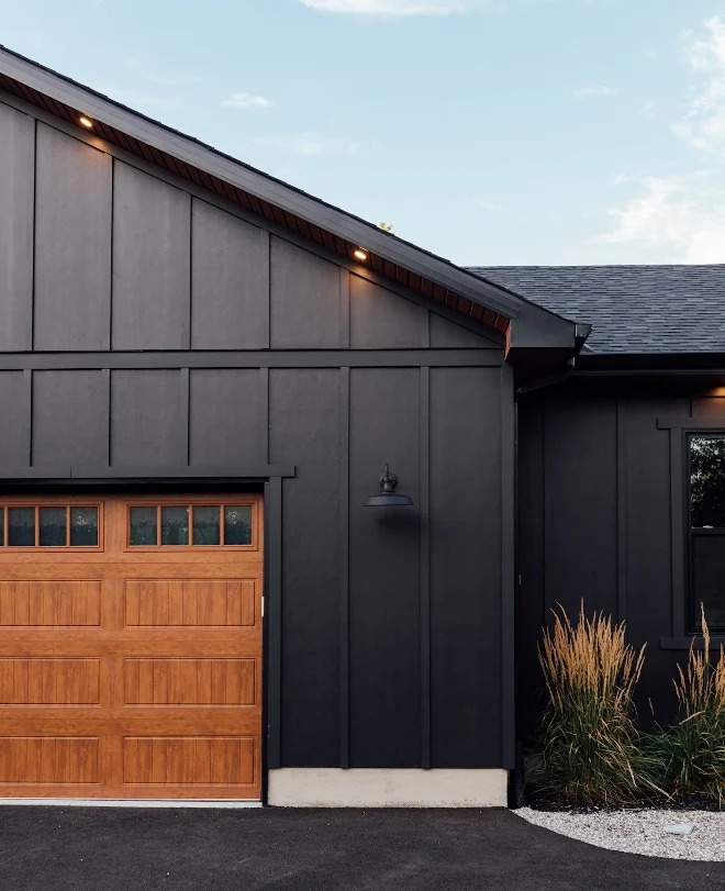 Black exterior paint color with black roof and a wood accented garage.